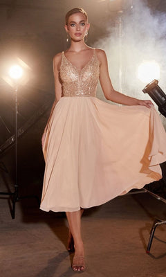A woman stands under studio lights holding one side of her Sheer-Bodice Tea-Length A-Line Party Dress CD0225, featuring a sleeveless, light beige v-neck design with a fitted glittery bodice and flowy skirt.