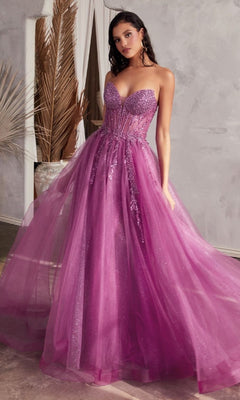 A woman stands indoors wearing the Strapless Sheer-Corset Long Prom Ball Gown CD0230—an elegant, floor-length purple tulle dress with a fitted, embellished bodice and flowing skirt.