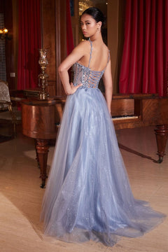 A woman stands indoors by a piano and red curtains, wearing the Ladivine CD0234 Glitter-Tulle Long Prom Dress with thin straps, an embellished sweetheart bodice, and a sparkly floor-length glitter-tulle overlay.