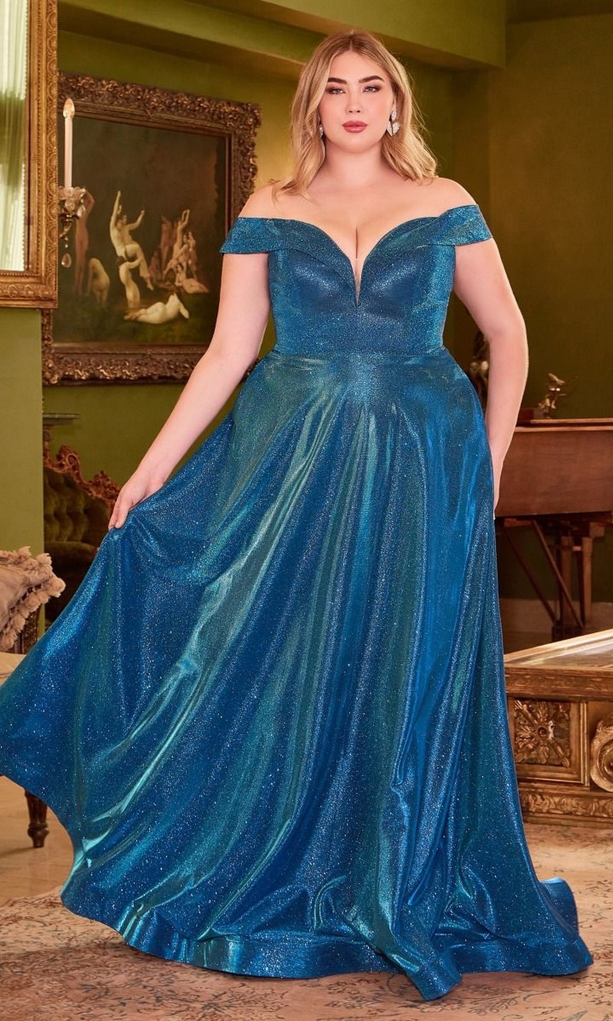 A woman showcases the Plus-Size Long Metallic Lace-Up Prom Dress CD210C indoors, standing by green walls and framed artwork. The shimmery, floor-length gown adds elegance to this formal setting.