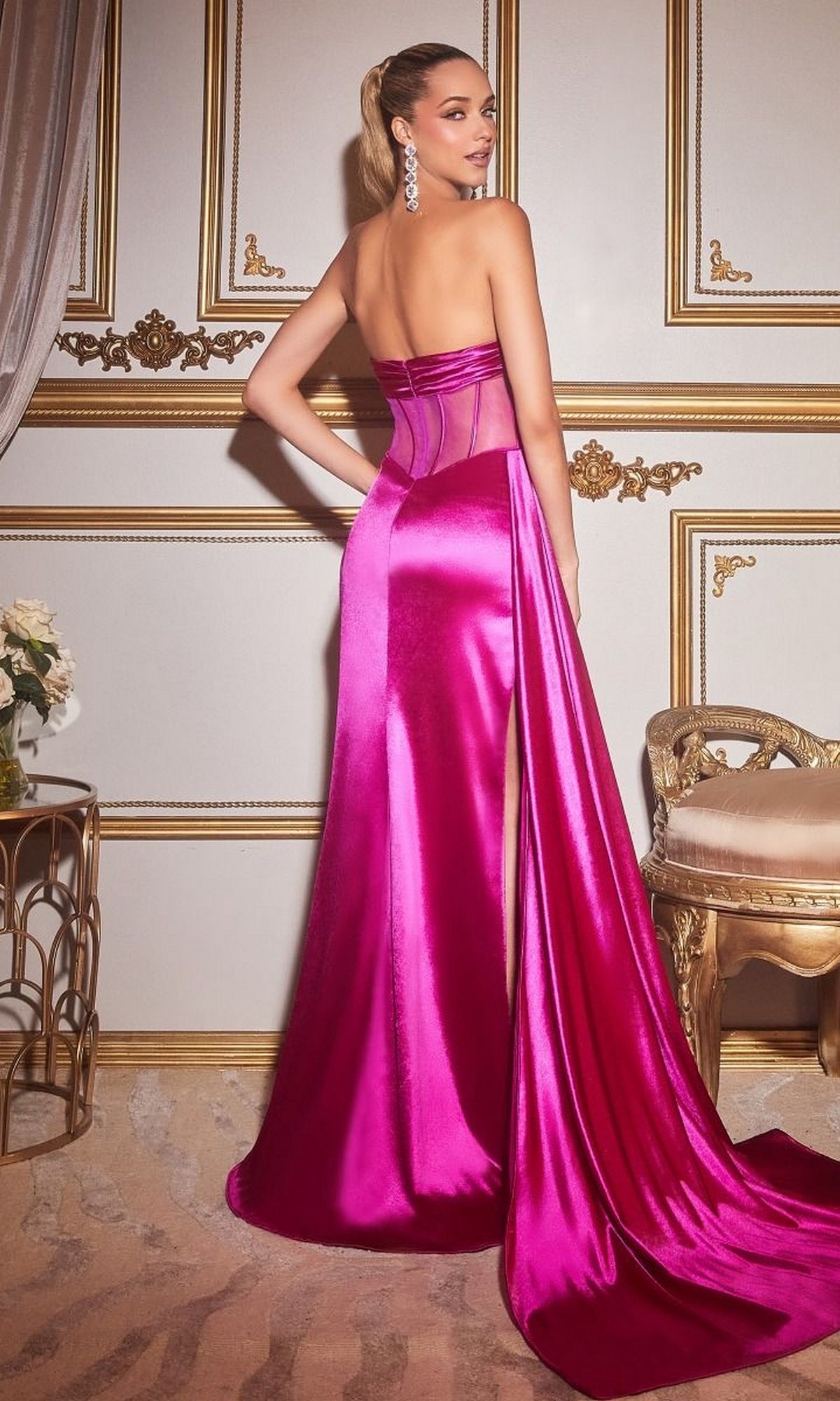 A woman stands in an ornate room wearing the Sheer-Bodice Sexy Long Strapless Prom Dress CD269 in bright pink satin, with a flowing train, looking over her shoulder.
