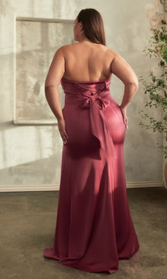 A woman in the Lace-Up Plus-Size Strapless Long Prom Dress CD326C stands with her back to the camera in a softly lit room, showcasing the gown's mauve hue, corset-style bodice, lace-up back, and delicate bow detail.