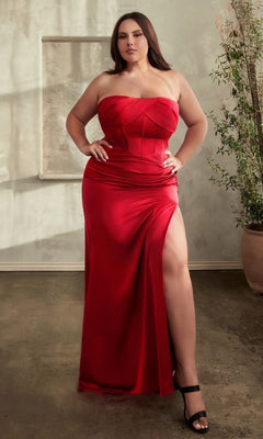 A woman stands indoors on a concrete floor beside a potted plant, wearing the Lace-Up Plus-Size Strapless Long Prom Dress CD326C with a corset-style bodice and thigh-high slit.