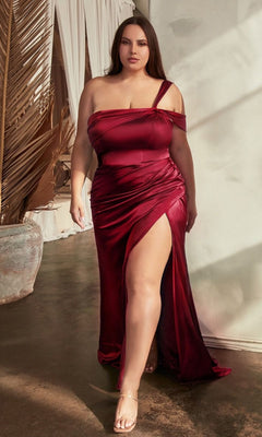 A woman in the One-Shoulder Plus-Size Long Prom Dress CD327C stands indoors near a sunlit wall and dried palm leaves.