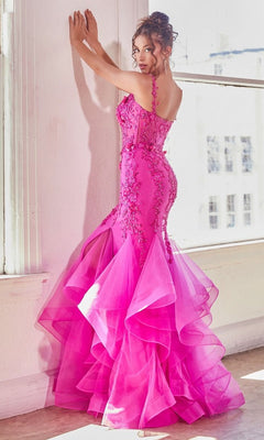 A woman stands by a white wall and window in the Bright Fuchsia Pink Long Mermaid Prom Dress CD331, featuring a ruffled floor-length skirt, floral embellishments, and elegant beaded lace appliqué.