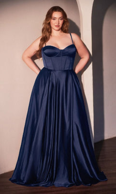 A woman stands indoors wearing the Ladivine CD337C Plus-Size Long A-Line Prom Dress, a navy blue satin gown with thin straps and a fitted bodice, her hands resting on her hips.