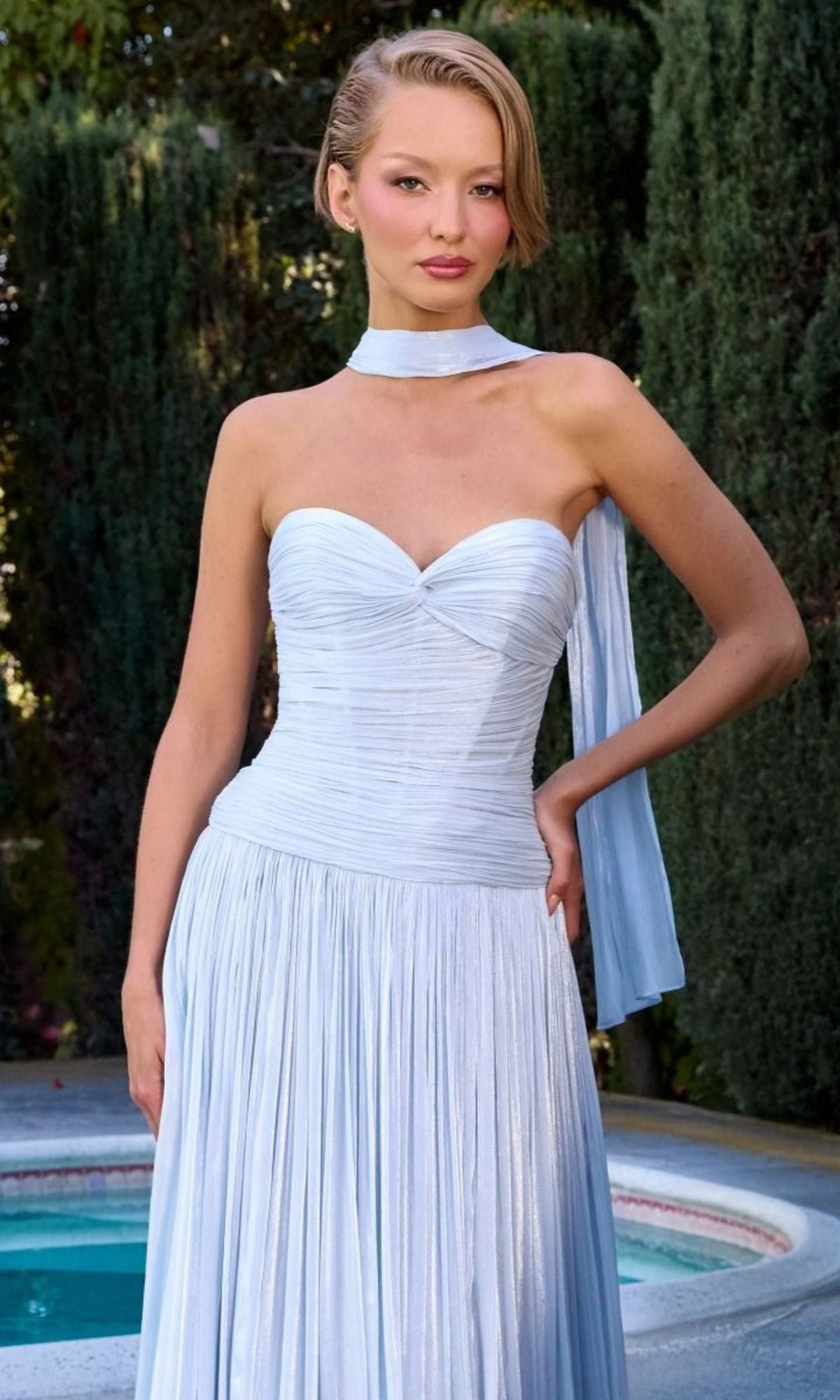 A woman stands by a pool wearing the Ladivine CD414 long prom dress in sky blue with a matching scarf; trees and shrubs are visible in the background.