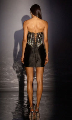 A woman faces away, wearing the Ladivine CD645 short homecoming dress featuring a strapless design, lace-up back, embellished corset bodice, and fitted satin skirt, styled with silver high heels.