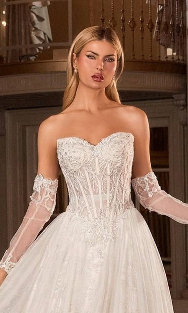 A woman stands indoors in an elegant setting, wearing the Ladivine CD717W long wedding dress, featuring a strapless design with beaded lace appliques and sheer lace sleeves.