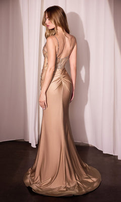 A woman stands facing away in front of white curtains, wearing the Ladivine CD779 Bead Sheer Bodice Long Prom Dress—an elegant champagne gown with a fitted bodice and low back.