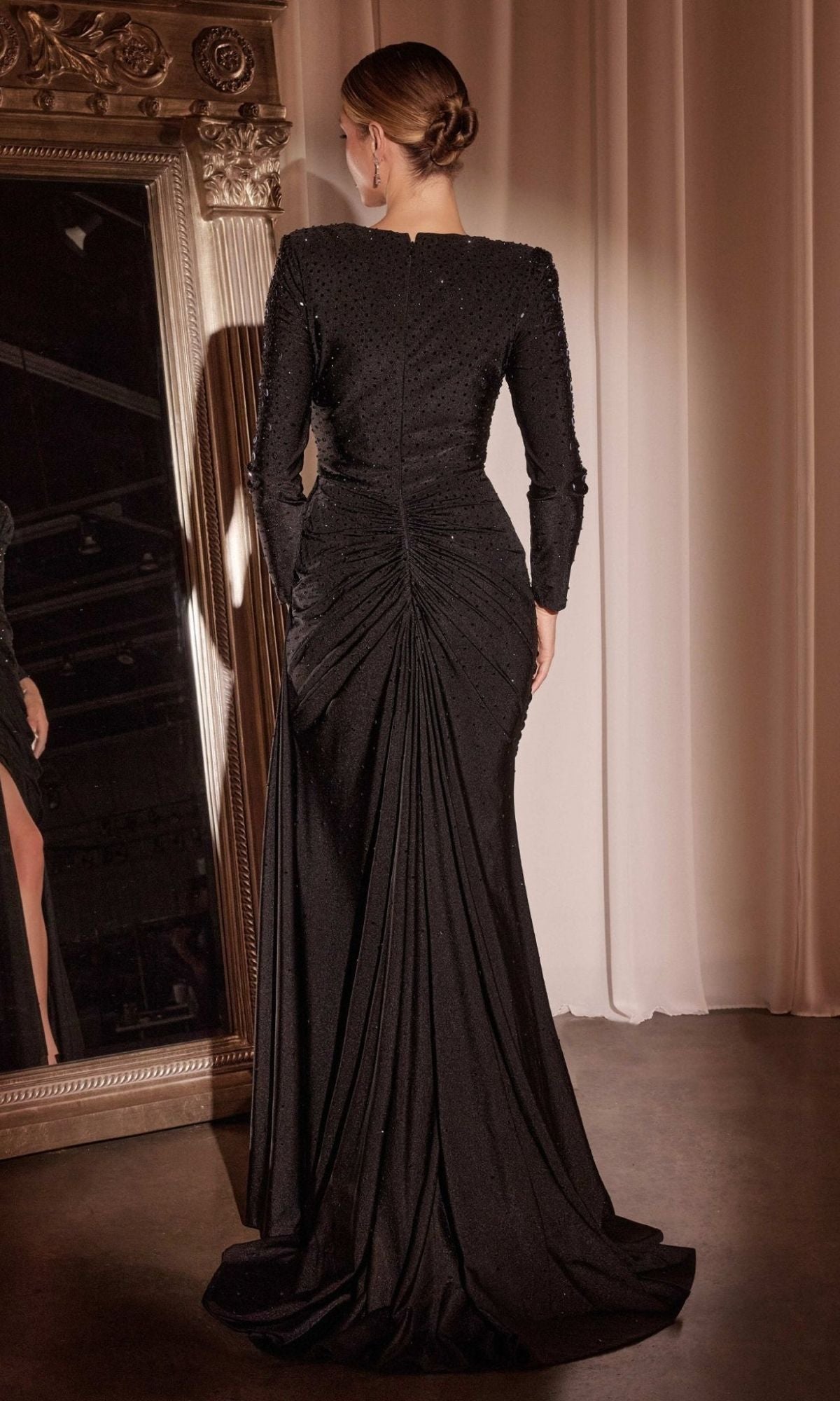 A woman with an elegant updo models the CLCD788 Long Sleeve Long Beaded Prom Dress, featuring a textured, ruched back, as she stands before a large ornate mirror.