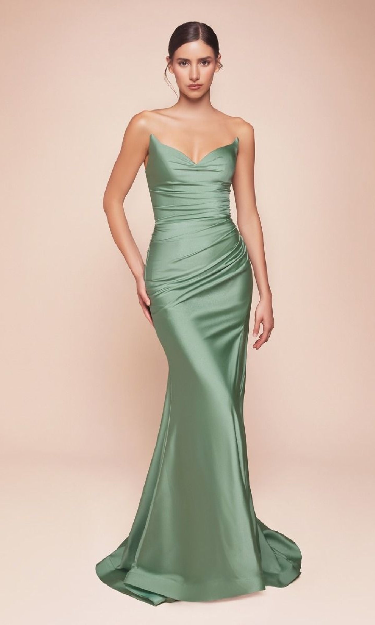 A woman faces forward in the sage green Ladivine LCD791 Lace-Up Strapless Long Prom Dress, floor-length and light green satin with a sweetheart neckline and booty-contouring ruching. The background is plain, light beige.