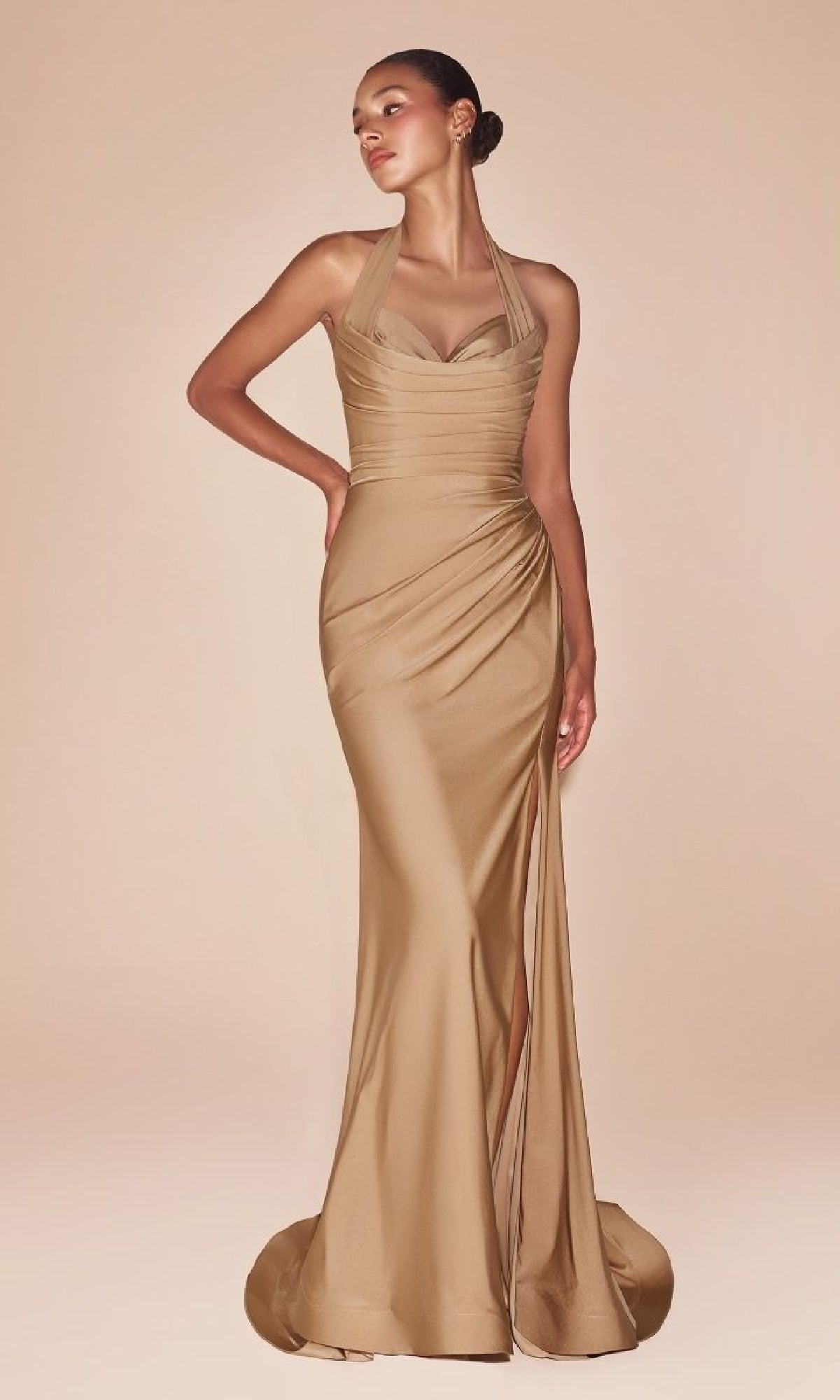 A woman poses against a beige background wearing the Classic Long Halter Prom Dress: CLCD796, a fitted, floor-length gold gown featuring a halter neckline and ruched details.