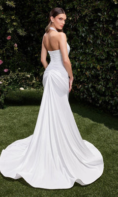 A woman in the Ladivine CD796W Long White Halter Prom Dress stands on grass, facing away, surrounded by lush greenery.