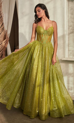 A woman indoors wears the Sheer-Bodice Long A-Line Shimmer Prom Dress CD832, a floor-length sparkling green gown with a structured bodice and spaghetti straps, elegantly holding out part of its skirt.