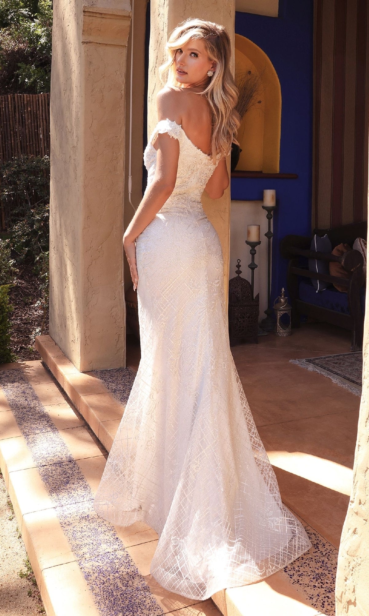 A woman in the Ladivine CD929 long off-white wedding dress stands on a tiled patio, looking back over her shoulder.