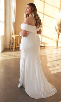 A woman wearing the Ladivine CD930C Long Plus-Size Bridal Dress stands in a sunlit room, elegantly framed by a stool and pampas grass.