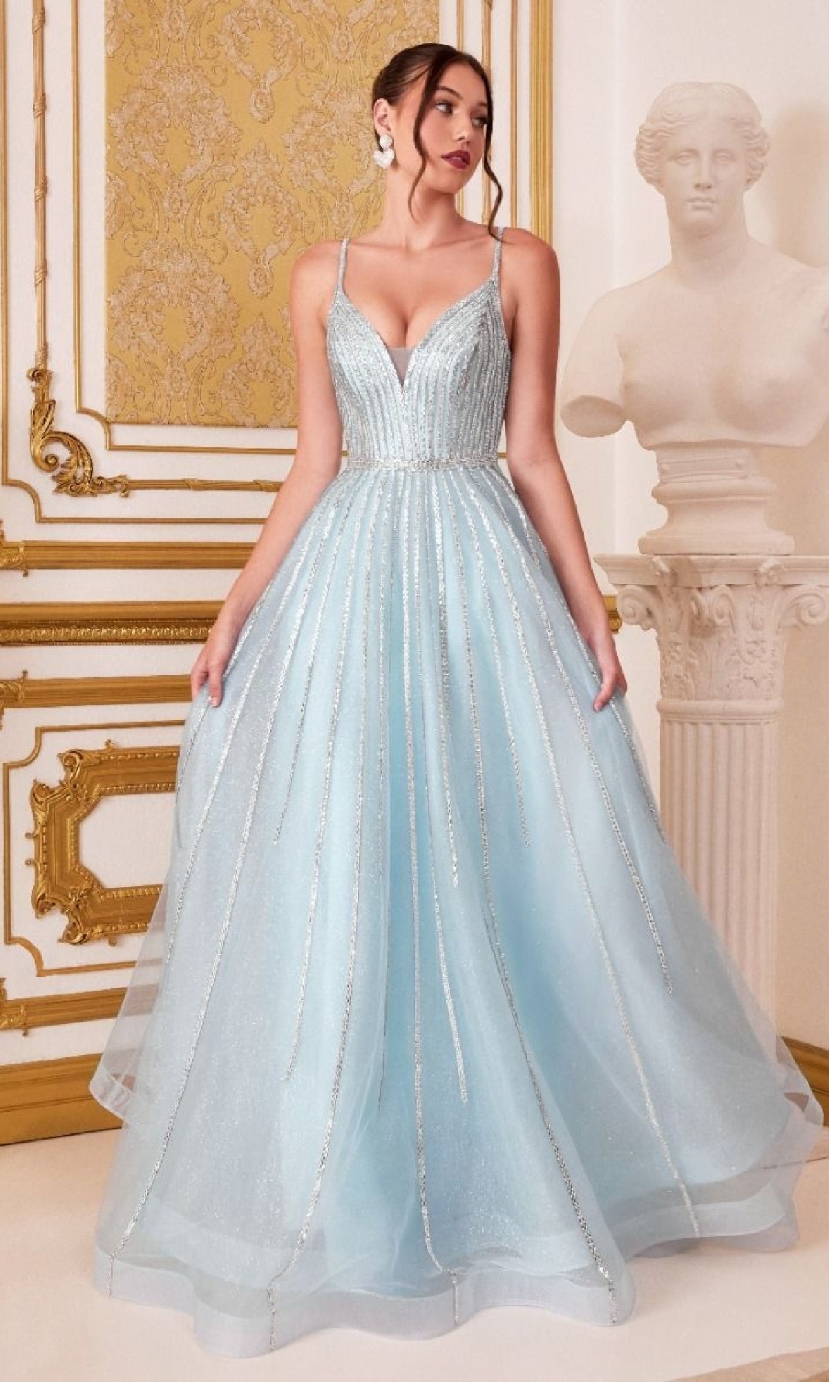 A woman in the Glitter-Tulle Long Prom Dress: Ladivine CD940, a light blue, floor-length A-line gown with thin straps, stands in an ornate room beside a white classical statue.