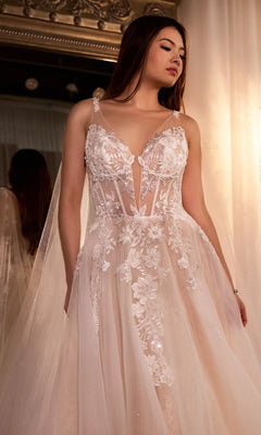 A woman wearing the Ladivine CDS476W Long Wedding Dress, a sleeveless sheer lace gown with floral appliqués, stands indoors in front of a mirror.