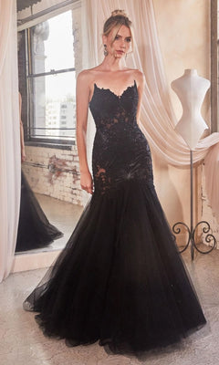 A woman wearing the Strapless Long Lace Mermaid Prom Dress CDS482 stands indoors by a dress form and large window, the black mermaid-style gown featuring sheer and lace details that capture its elegant, embroidered evening style.