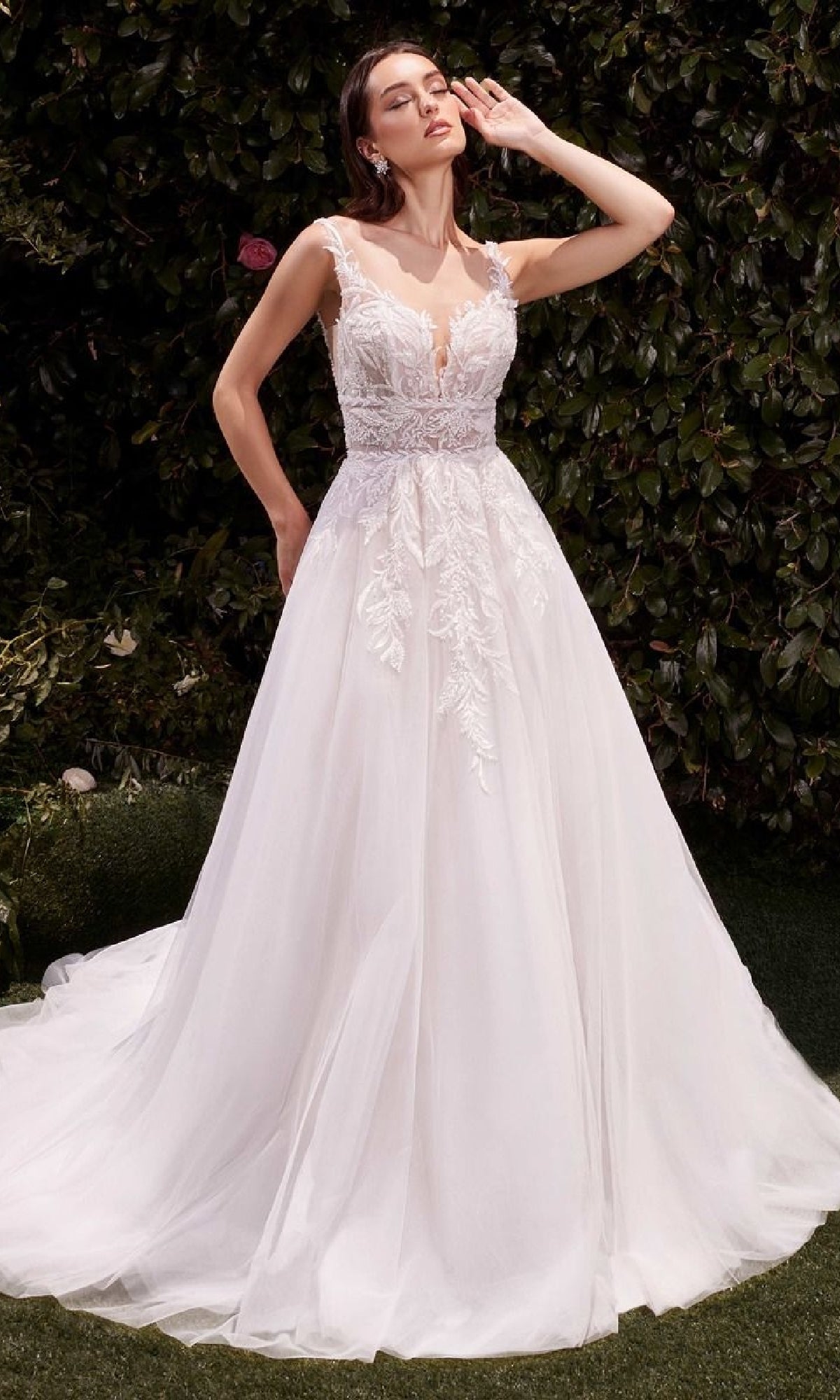 A woman poses outdoors in the Ladivine CDS511W long wedding dress, featuring a lace-embroidered bodice and full tulle skirt, with one hand gracefully raised near her face.