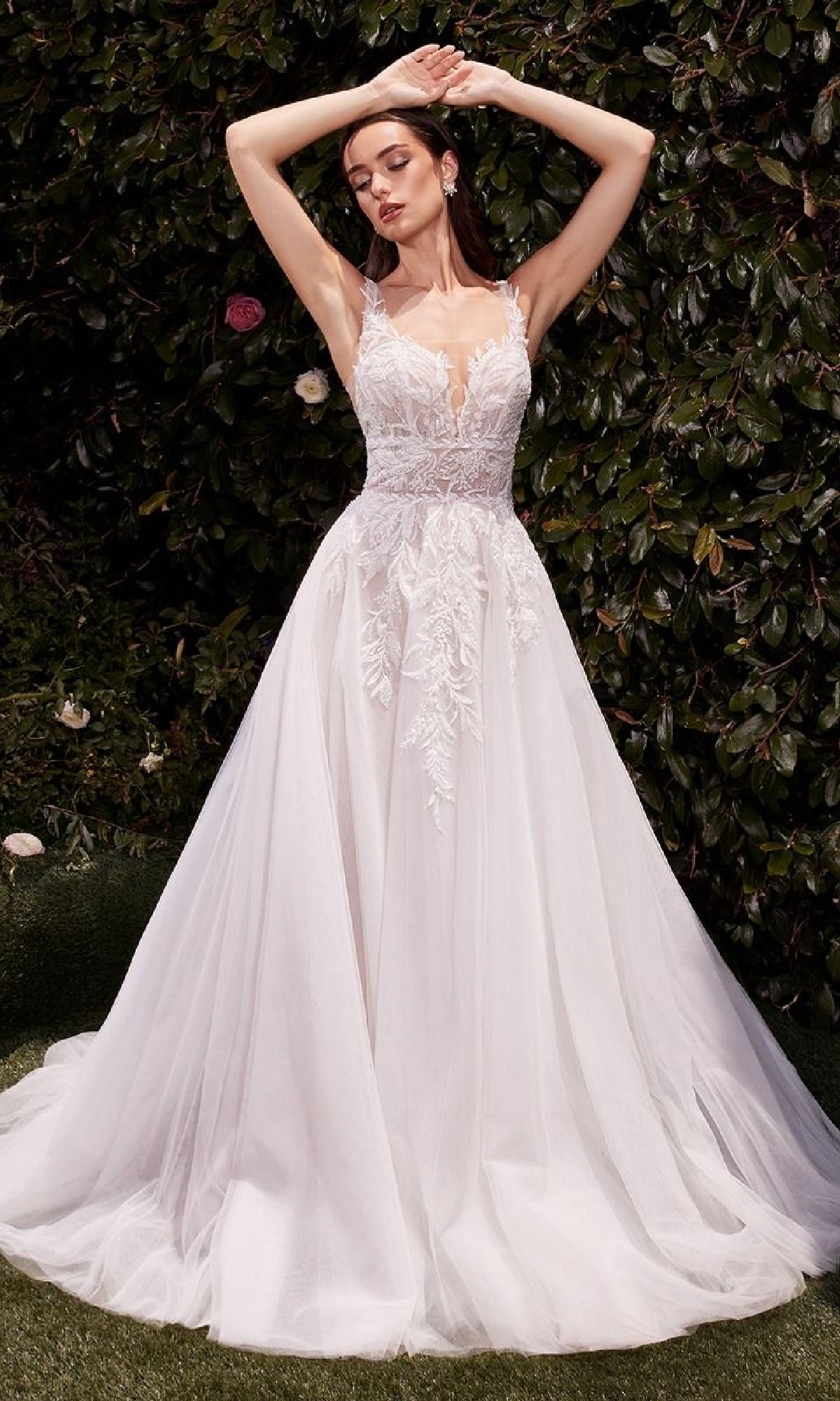 A woman poses outdoors in the Ladivine CDS511W long wedding dress, featuring a lace-embroidered bodice and full tulle skirt, standing before leafy greenery.