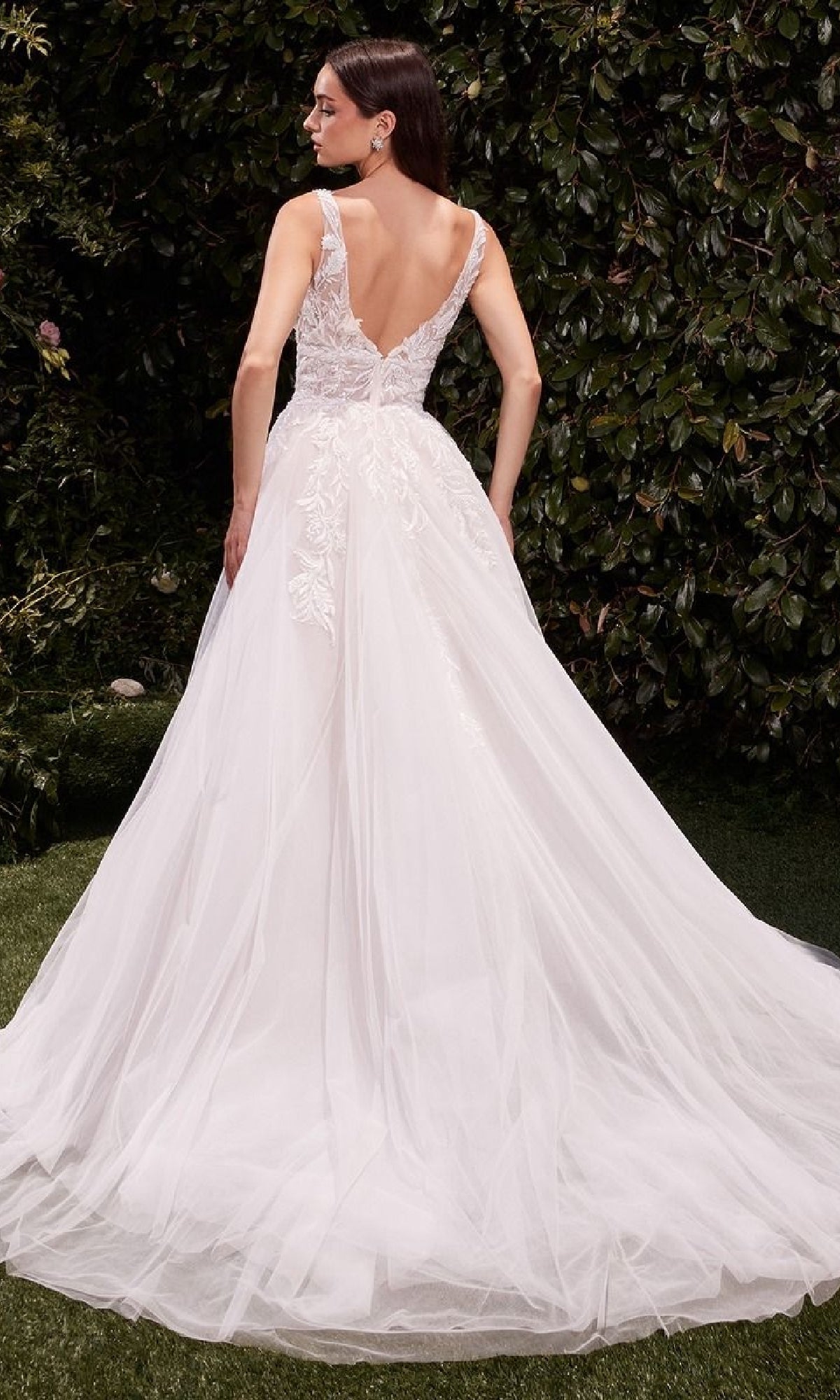 A woman in the Ladivine CDS511W long wedding dress with a lace-embroidered bodice and flowing tulle skirt stands outdoors amid green foliage.