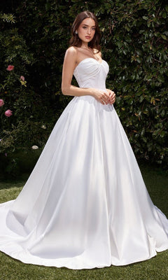 A woman stands outdoors on grass, surrounded by lush green foliage, wearing the Ladivine CDS512W White Satin Formal Ball Gown.