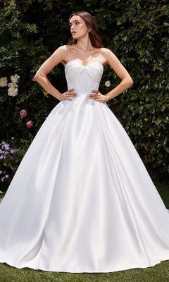 A woman wearing the Ladivine CDS512W White Satin Formal Ball Gown stands outdoors amid lush green foliage and blooming flowers.