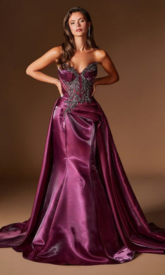 A woman stands against a plain brown background wearing the Ladivine CDS568 long prom dress in Plum Noir, featuring a strapless, floor-length satin design with hand-beaded embellishments on the bodice.