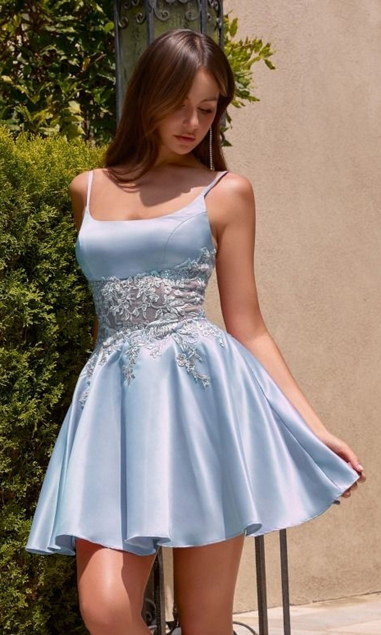 A young woman stands outdoors near greenery and a wall, wearing the Ladivine CH2613 short homecoming dress in blue—a sleeveless, light A-line style with lace detailing.