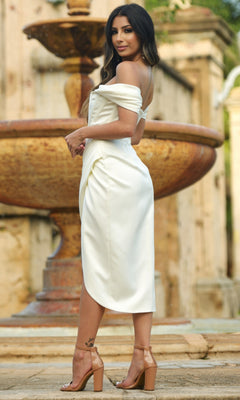 A woman in the Velvi Off-the-Shoulder Short Party Dress Cindi and nude heels stands sideways by a large rustic outdoor fountain.