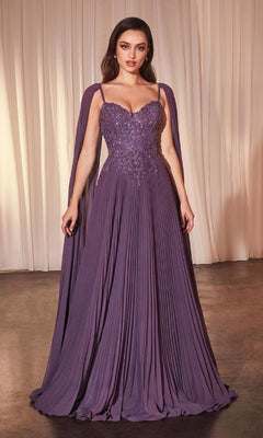 A woman stands indoors against light drapes, wearing the Ladivine CJ937 Shoulder-Cape Long Prom Dress featuring a pleated skirt, beaded sweetheart bodice, and matching shoulder cape.