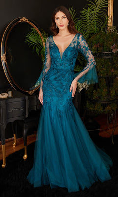 A woman in the Bell-Sleeve Peacock Blue Long Formal Dress CM327 with sheer lace sleeves and elegant embroidery stands indoors by a mirror and lush greenery.
