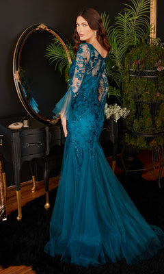 A woman in the Bell-Sleeve Peacock Blue Long Formal Dress CM327 with lace applique stands before a vintage mirror and black vanity, surrounded by lush plants in an elegant room.