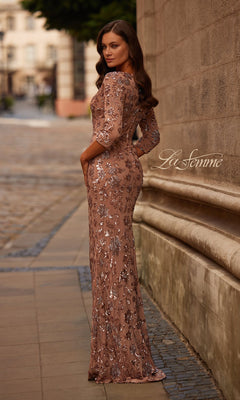 Woman outdoors in the Long Brown Sequin Formal Dress: La Femme 32613, light brown with silver sequin details, looking over her shoulder near a stone wall.