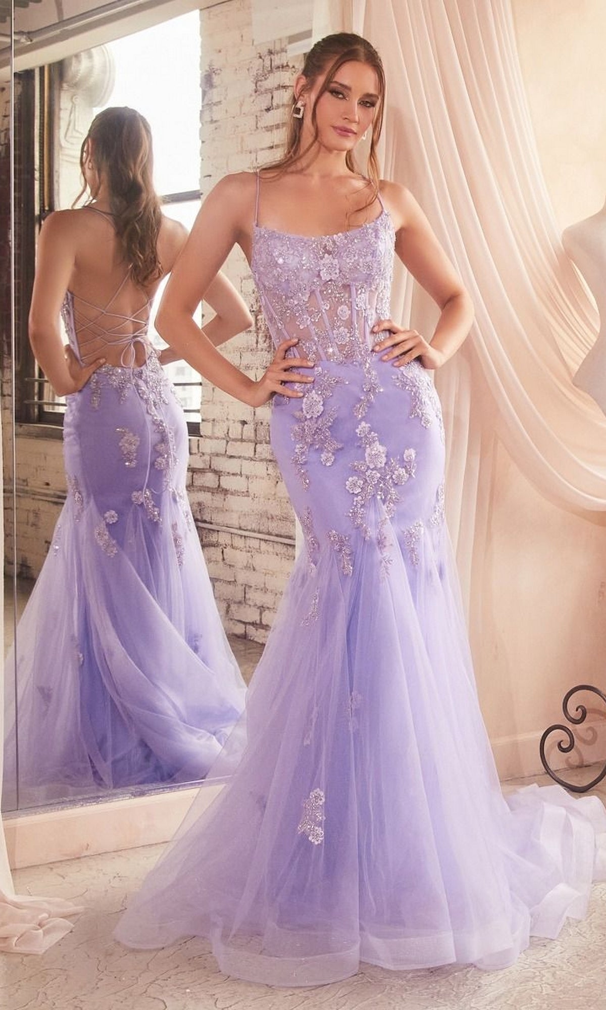 A woman stands in front of a mirror wearing the Long Pastel Floral Mermaid Prom Dress D145, a fitted lavender gown with appliqués, a sheer bodice, thin straps, and an open-back formal mermaid design.