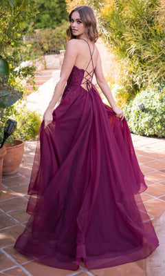 A woman in the Velvi Long Sweetheart A-Line Prom Dress Dani, a deep magenta, floor-length lace gown with a lace-up back, stands on a tiled patio holding her dress and looking over her shoulder.