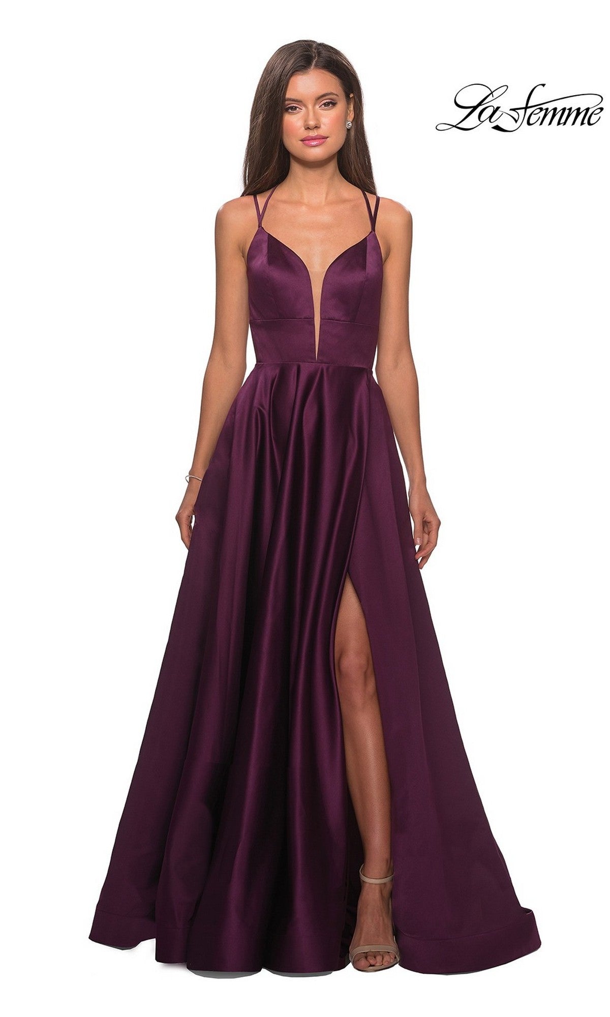 A woman stands against a white background in the La Femme Deep V-Neck Long A-Line Prom Dress 26994, featuring sleeveless design, floor-length deep purple satin fabric, a plunging neckline, high slit, and open back.