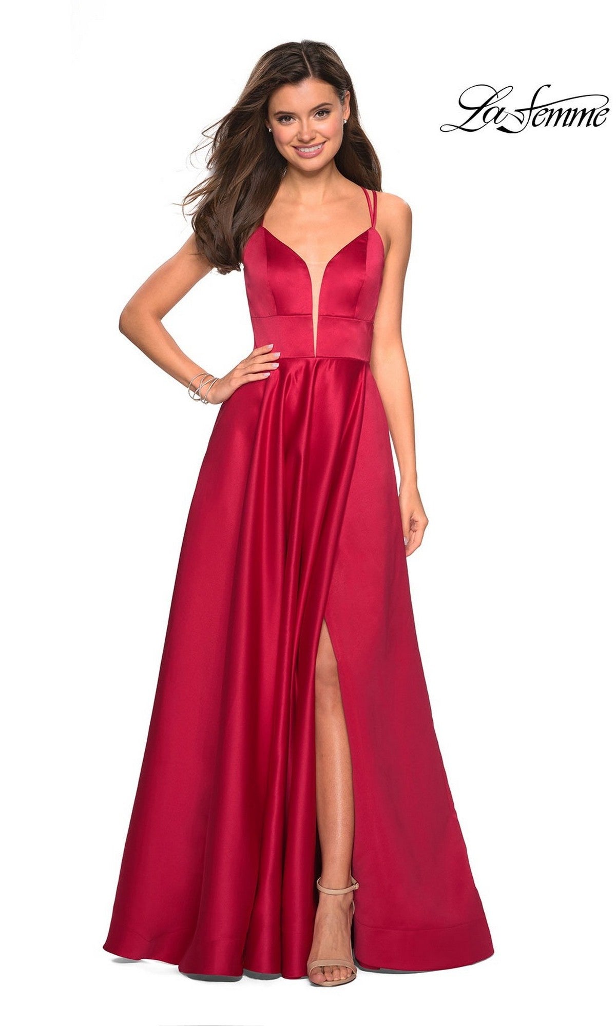A woman wears the La Femme Deep V-Neck Long A-Line Prom Dress 26994—sleeveless, deep red with spaghetti straps, an open back, high slit, and deep V-neckline—standing against a plain white background.
