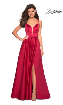 A woman wears the La Femme Deep V-Neck Long A-Line Prom Dress 26994—sleeveless, deep red with spaghetti straps, an open back, high slit, and deep V-neckline—standing against a plain white background.