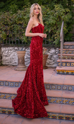 A woman stands on patterned tiled steps with lush greenery behind her, wearing the Velvi Clear-Strap Long Sequin Prom Dress Dover, a strapless, floor-length red designer dress adorned with sequins.