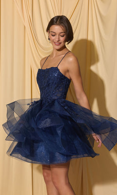 A woman wears the Short Homecoming Dress: Eureka EK137—sleeveless, sparkly navy blue with a full tulle skirt—standing before draped yellow fabric.