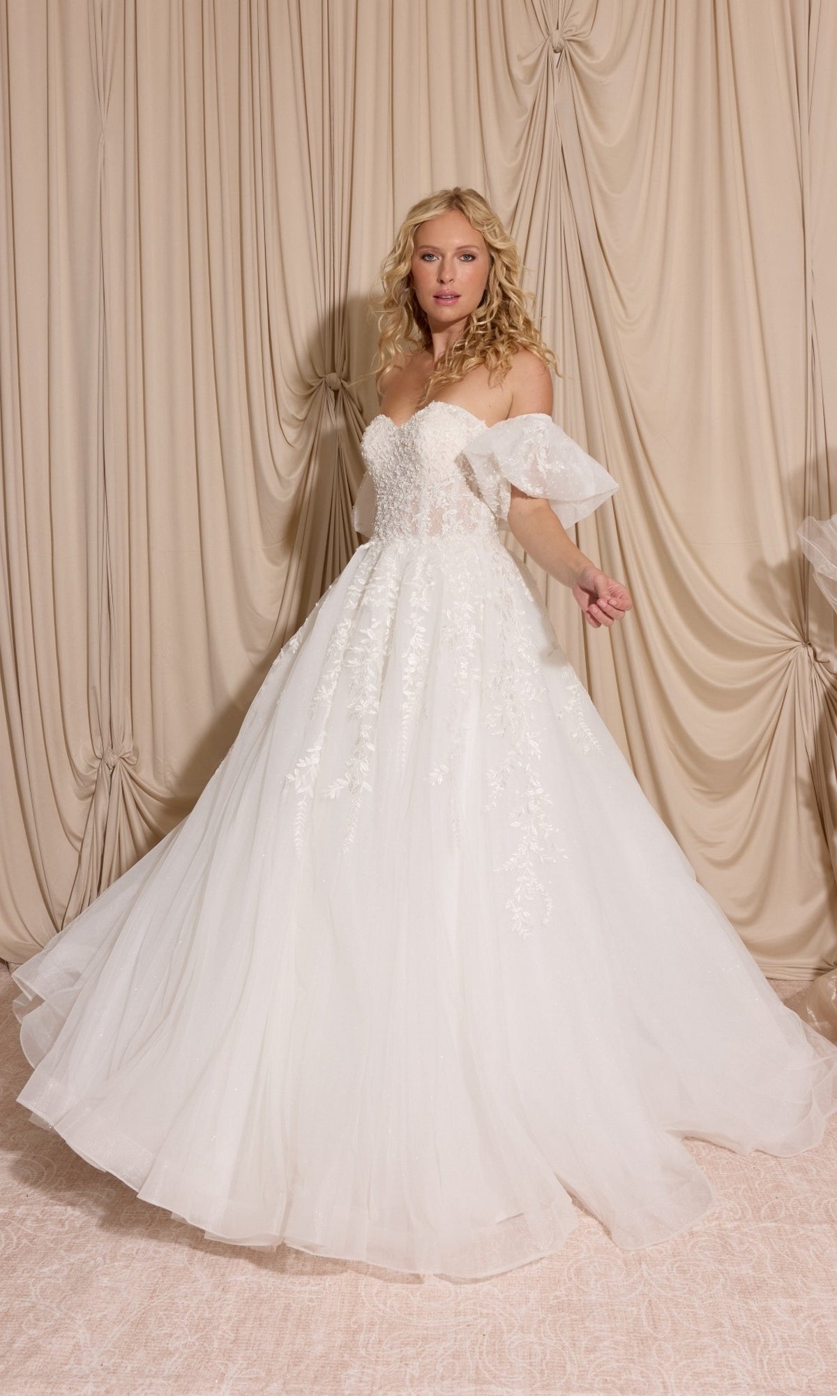 Woman in the Long Wedding Dress: Eureka EK155 in off white with lace details and detachable puff sleeves stands before beige curtains, holding out her elegant gown.