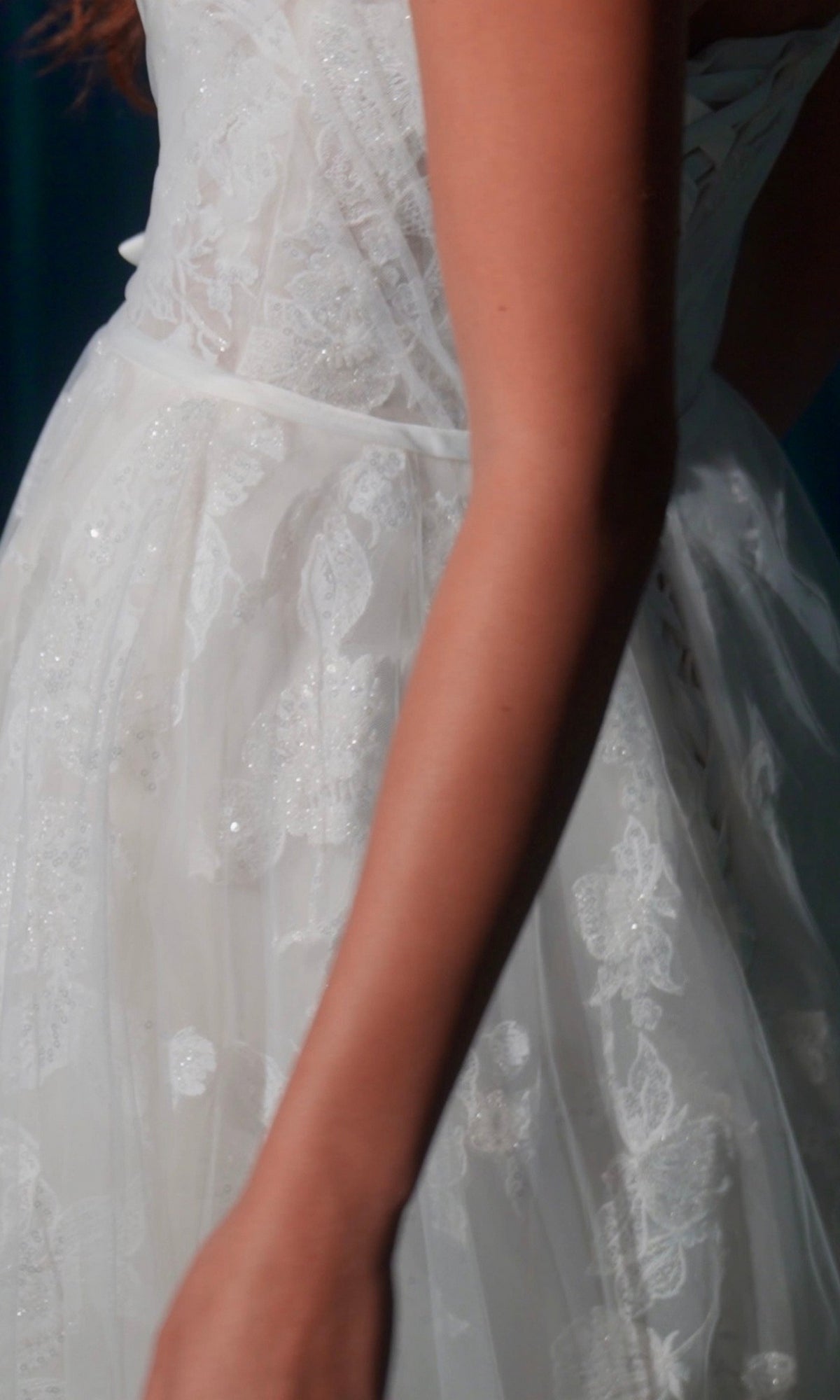 Close-up of a person in the Long Wedding Dress: Eureka EK165, featuring white lace with floral patterns and delicate appliques against a dark background.