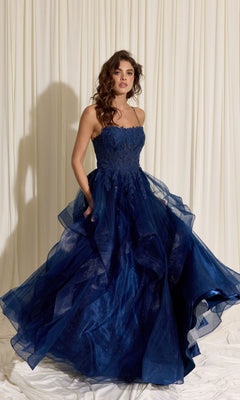 A woman in the Eureka EK167 Long Prom Dress in navy, featuring a strapless floral lace corset and layered tulle A-line skirt, stands before cream draped fabric.