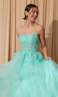 A woman in the Eureka EK167 long prom dress with a light blue glitter tulle skirt, floral lace corset bodice, and thin straps stands smiling in front of beige curtains, holding her dress.