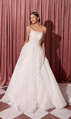 A woman in the Long Wedding Dress: Eureka EK175 with a strapless ball-gown silhouette stands on a checkered floor by pink curtains, looking aside and holding her dress.