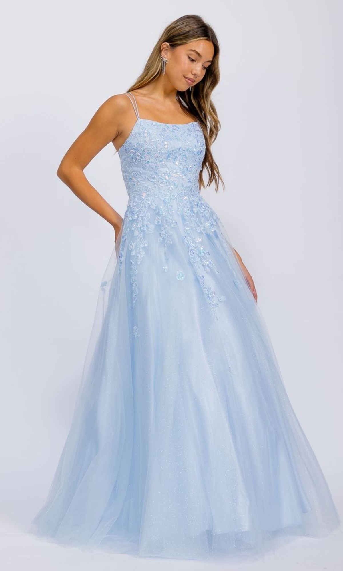 A woman in the Bahama Blue Floral-Lace Long Prom Ball Gown (Eureka EK197) with spaghetti straps and floral appliqué stands against a plain white background.