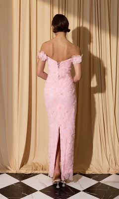 A woman stands on a black and white tiled floor, facing away, wearing the Eureka EK205 long prom dress in pale pink lace with 3D floral appliqué, off the shoulder design, and back slit. Cream curtains are draped behind her.